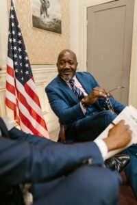 Two professionals in discussion by an American flag in an office setting.